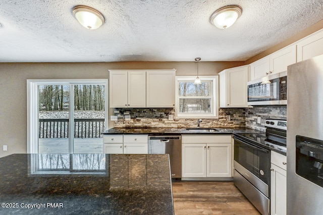 kitchen with decorative backsplash, appliances with stainless steel finishes, wood finished floors, pendant lighting, and a sink