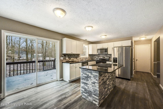 kitchen featuring white cabinets, dark wood finished floors, dark countertops, appliances with stainless steel finishes, and backsplash