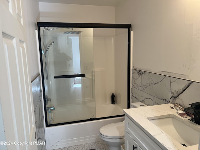 bathroom with toilet, shower / bath combination with glass door, tile walls, and vanity