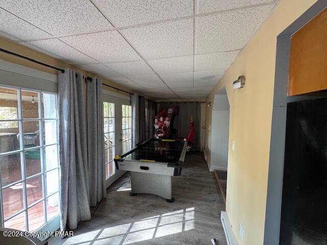 recreation room with baseboards, a drop ceiling, a baseboard radiator, french doors, and light wood-type flooring