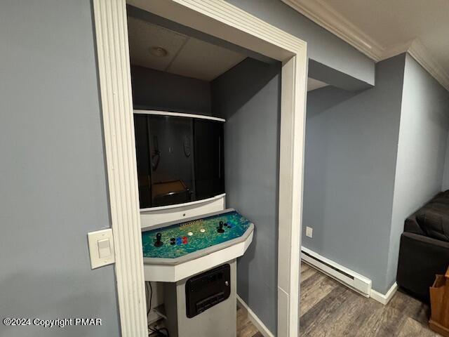 interior space featuring crown molding, baseboard heating, wood finished floors, and baseboards