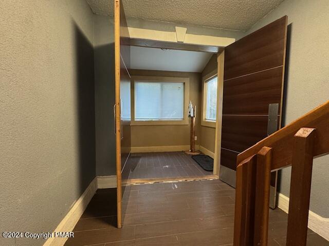 hall with vaulted ceiling, a textured wall, a textured ceiling, and baseboards