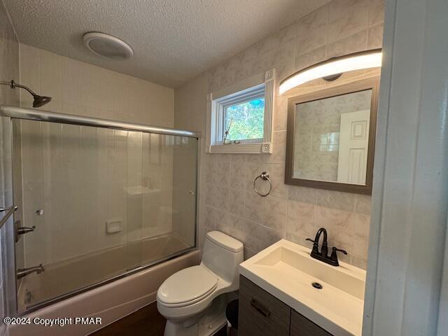 bathroom featuring tile walls, toilet, enclosed tub / shower combo, a textured ceiling, and vanity