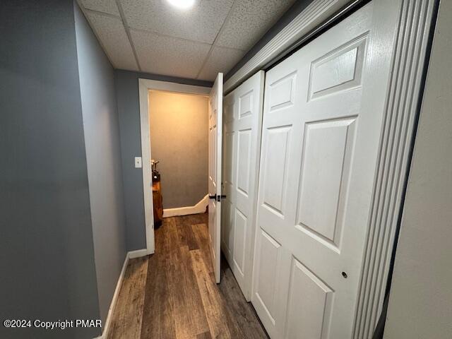 hall with a drop ceiling, dark wood finished floors, and baseboards