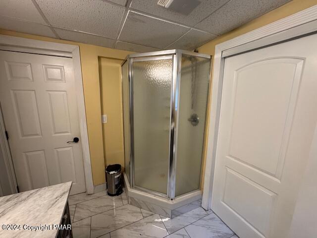 bathroom with marble finish floor, vanity, a shower stall, and a paneled ceiling