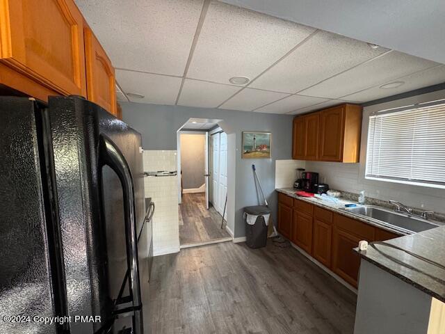 kitchen with dark wood-type flooring, freestanding refrigerator, brown cabinetry, and a sink