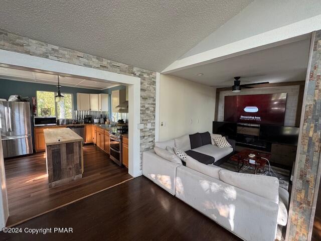 living area featuring lofted ceiling, dark wood-style flooring, ceiling fan, and a textured ceiling