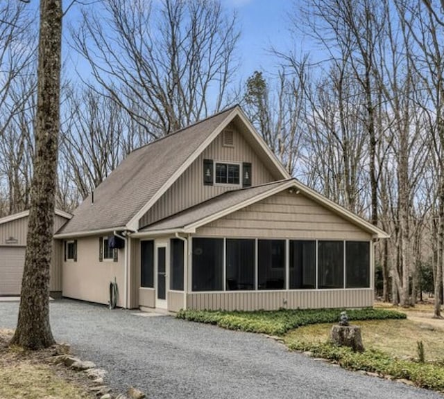 view of front of house with a sunroom, an outbuilding, driveway, and a shingled roof