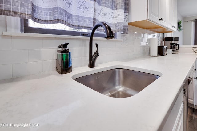 interior details with tasteful backsplash, light countertops, white cabinets, and a sink