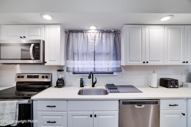 kitchen with appliances with stainless steel finishes, white cabinetry, a sink, and decorative backsplash