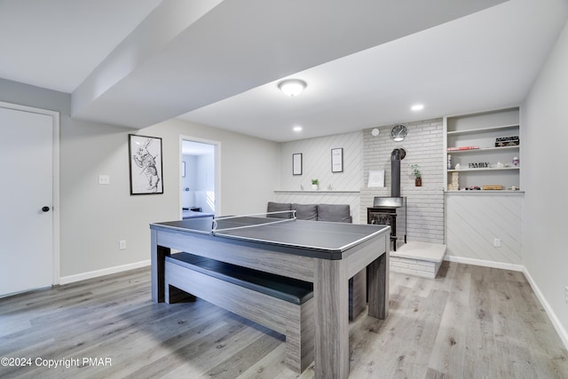 recreation room with a wood stove, baseboards, and light wood finished floors