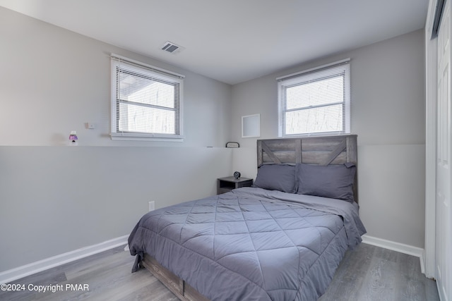 bedroom featuring baseboards, multiple windows, visible vents, and wood finished floors