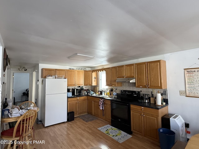 kitchen with black / electric stove, light wood finished floors, freestanding refrigerator, under cabinet range hood, and dark countertops