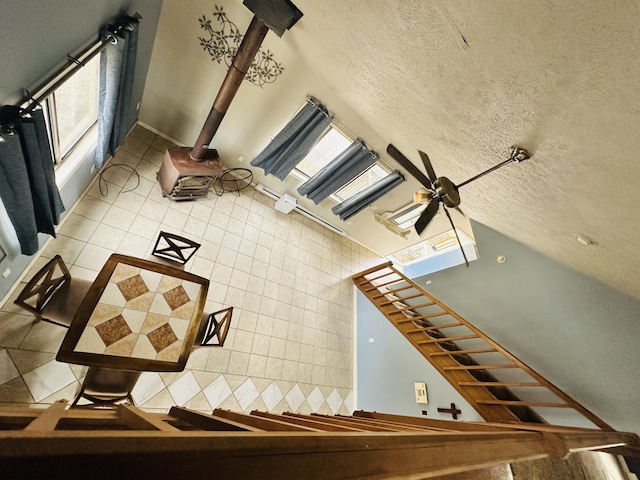 stairs with tile patterned floors, ceiling fan, a wood stove, and a textured ceiling