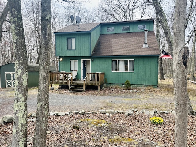 back of house with a storage shed, a deck, a shingled roof, and an outdoor structure