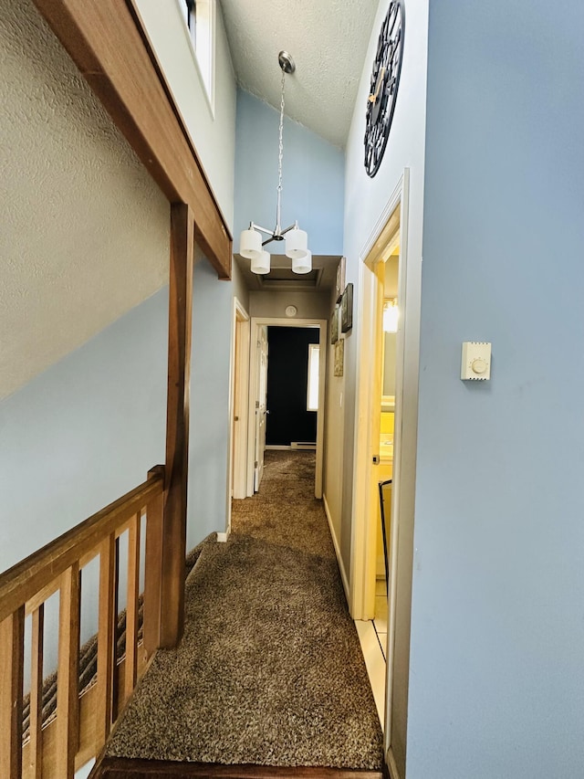 hallway featuring carpet flooring, a high ceiling, a notable chandelier, a textured ceiling, and baseboards