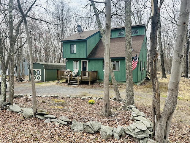 back of property with a wooden deck, a shingled roof, an outbuilding, and a shed