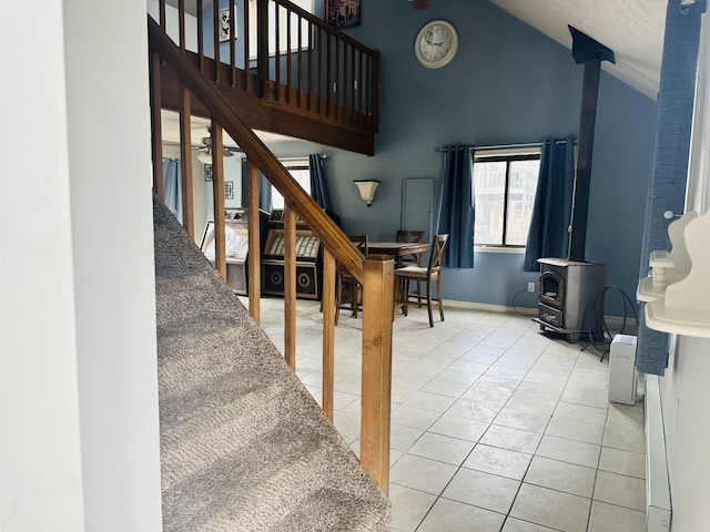 stairway with high vaulted ceiling, tile patterned flooring, and a wood stove