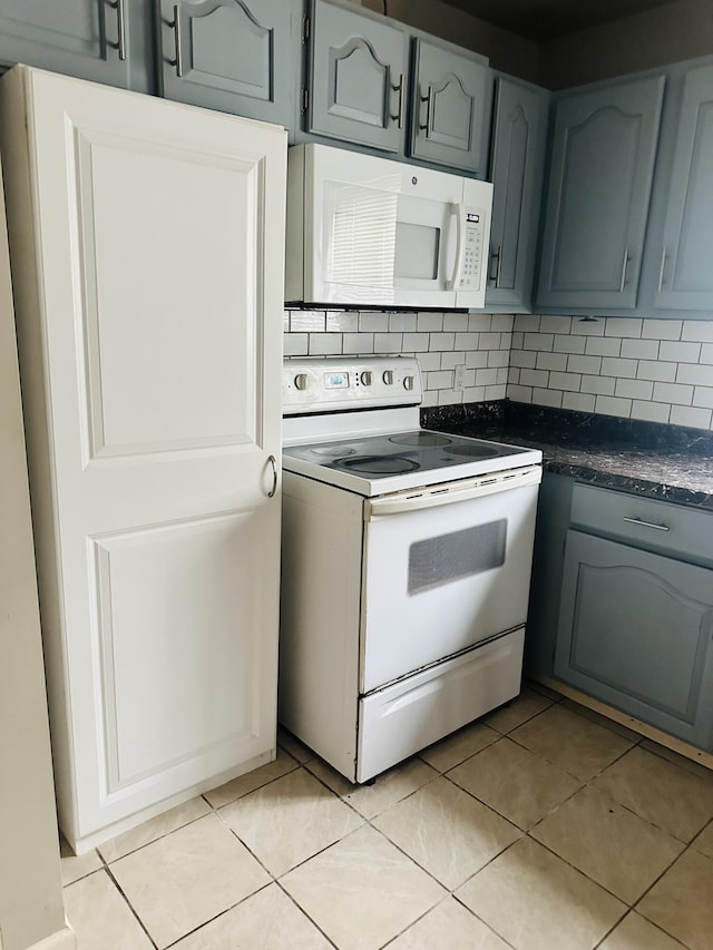 kitchen featuring white appliances, dark countertops, light tile patterned floors, and tasteful backsplash