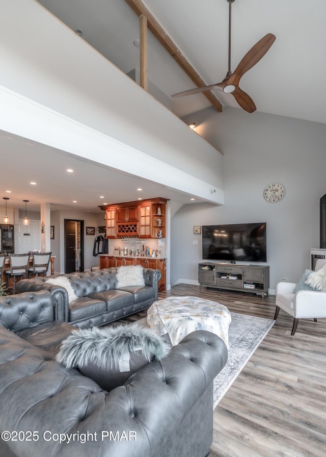 living area featuring baseboards, bar, wood finished floors, high vaulted ceiling, and a ceiling fan