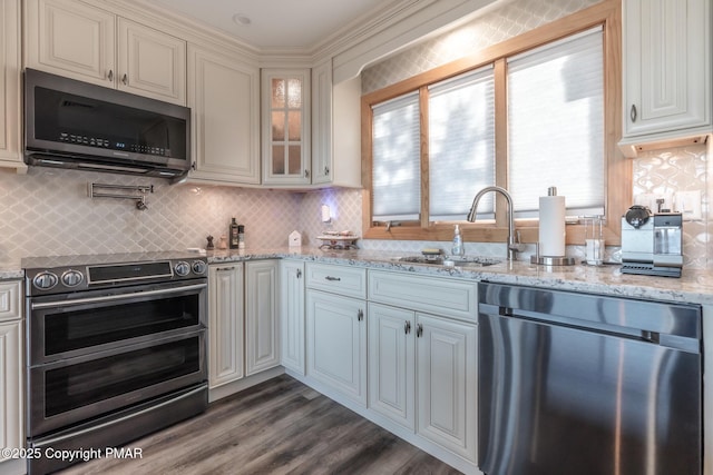 kitchen with glass insert cabinets, dark wood-type flooring, decorative backsplash, stainless steel appliances, and a sink