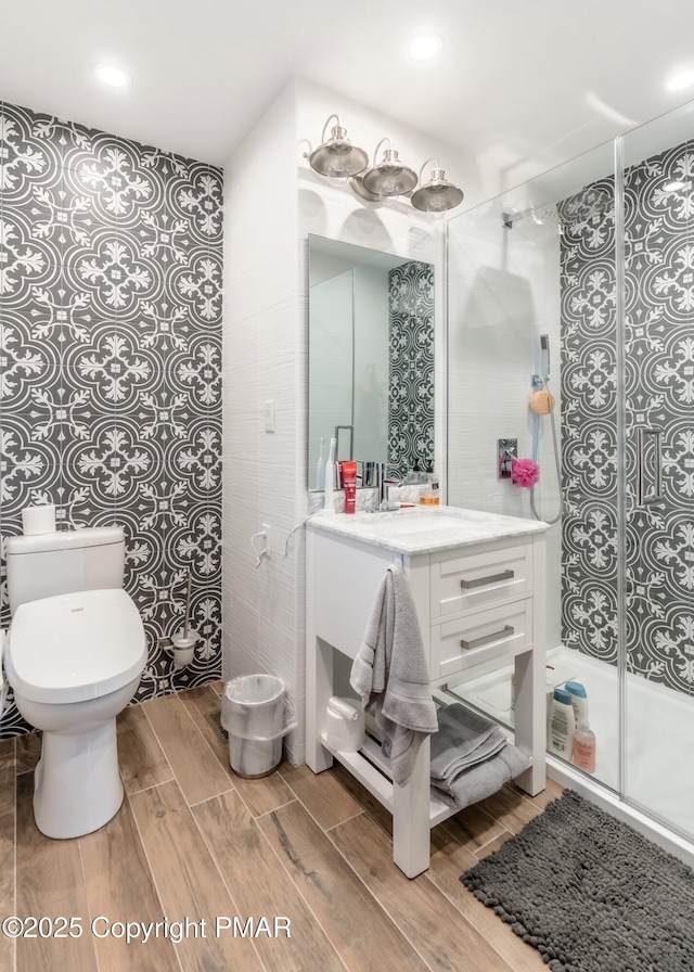 bathroom with wood finish floors, toilet, a stall shower, and vanity