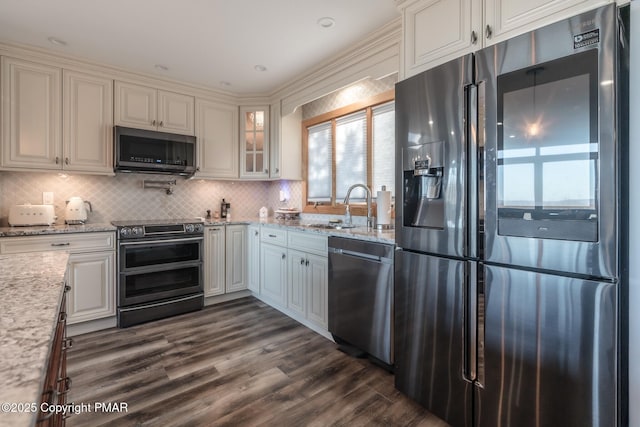 kitchen featuring a sink, backsplash, stainless steel appliances, light stone countertops, and dark wood-style flooring