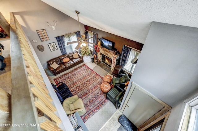 living area featuring a textured ceiling, high vaulted ceiling, a stone fireplace, and a ceiling fan