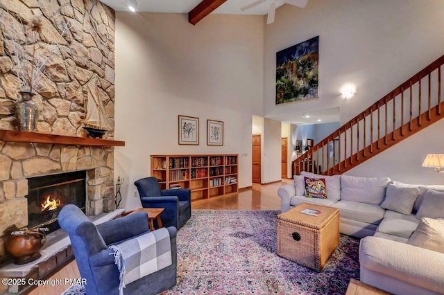 living room featuring beam ceiling, stairway, a towering ceiling, a stone fireplace, and wood finished floors