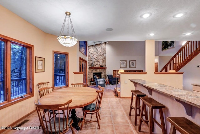 dining room featuring light tile patterned floors, recessed lighting, stairway, a stone fireplace, and baseboards