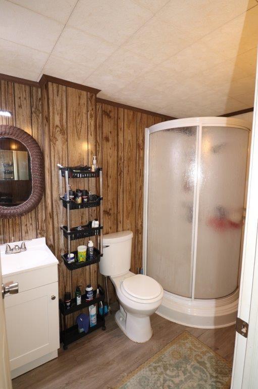 full bath featuring toilet, wood finished floors, vanity, wood walls, and a shower stall