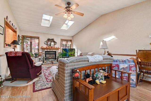 living area with lofted ceiling with skylight, a fireplace, ceiling fan, and light wood finished floors