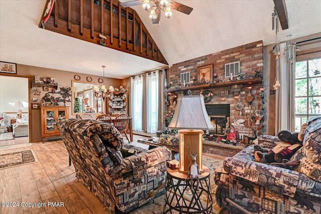 living room with lofted ceiling, wood-type flooring, a textured ceiling, a brick fireplace, and ceiling fan with notable chandelier