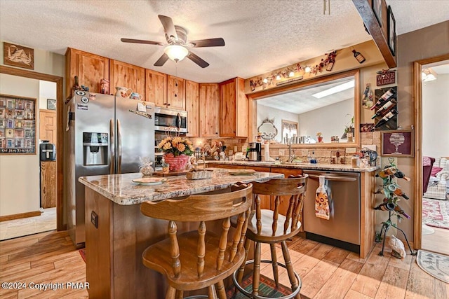 kitchen with appliances with stainless steel finishes, brown cabinetry, light wood-type flooring, and a sink