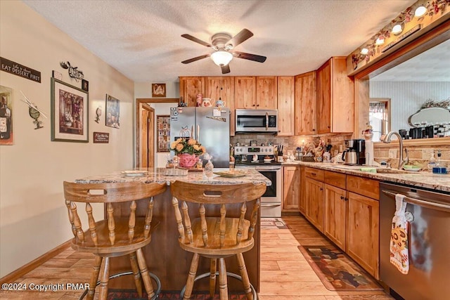 kitchen with a textured ceiling, stainless steel appliances, a kitchen island, backsplash, and light wood finished floors