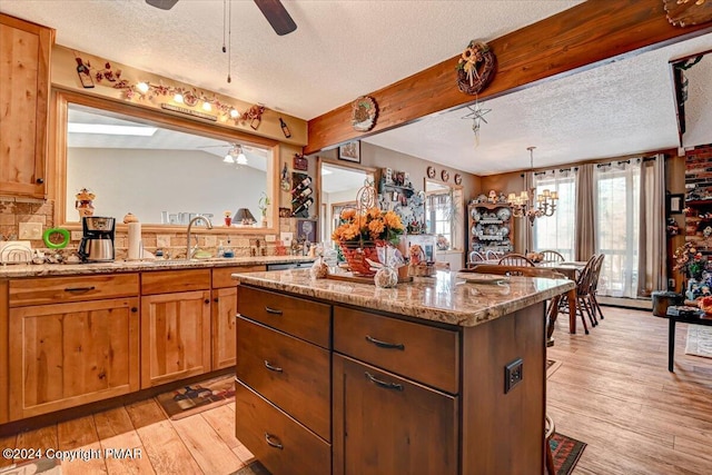 kitchen with a center island, a sink, light stone countertops, light wood-type flooring, and ceiling fan with notable chandelier