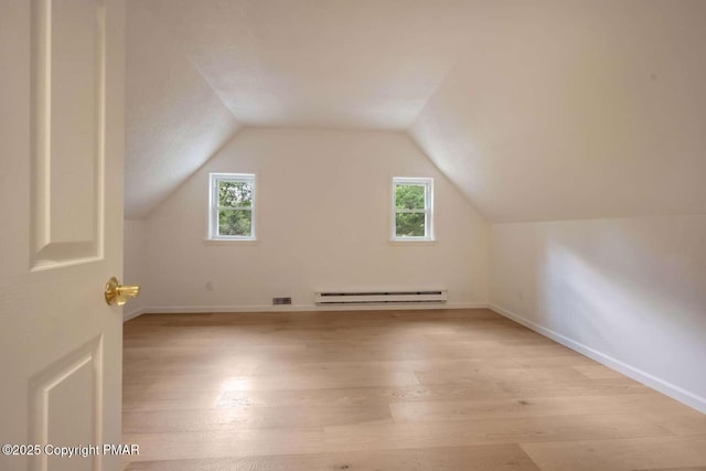 additional living space featuring vaulted ceiling, a healthy amount of sunlight, light wood-type flooring, and a baseboard heating unit