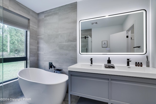 bathroom featuring double vanity, a shower, a soaking tub, a sink, and tile walls