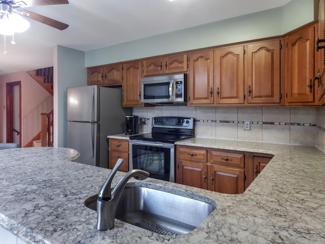 kitchen featuring light stone countertops, brown cabinets, tasteful backsplash, a sink, and stainless steel appliances