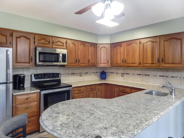 kitchen with a sink, a peninsula, brown cabinets, a ceiling fan, and appliances with stainless steel finishes