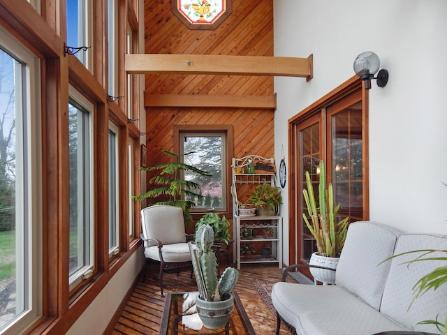 sunroom / solarium featuring a high ceiling, beamed ceiling, wood walls, and wood finished floors