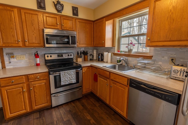 kitchen with dark wood-style floors, appliances with stainless steel finishes, brown cabinets, light countertops, and a sink