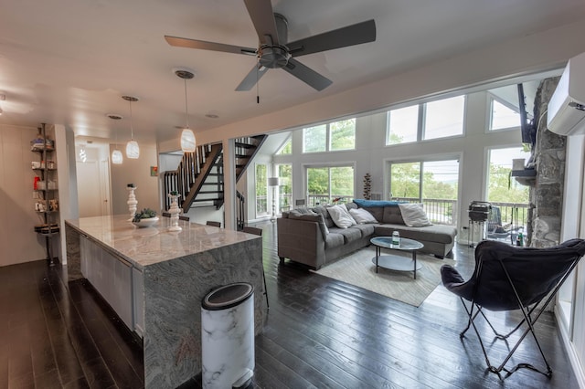 kitchen featuring dark wood-style flooring, a ceiling fan, light stone counters, hanging light fixtures, and a kitchen island