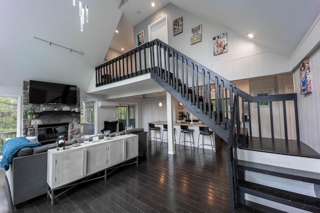 living area with hardwood / wood-style flooring, stairway, high vaulted ceiling, a fireplace, and rail lighting