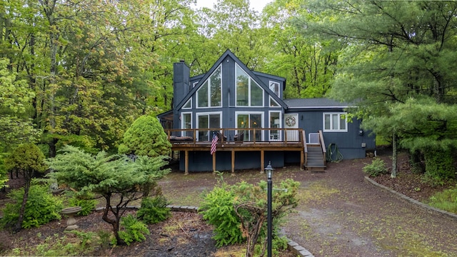 back of house featuring a wooden deck, a chimney, stairway, and a forest view