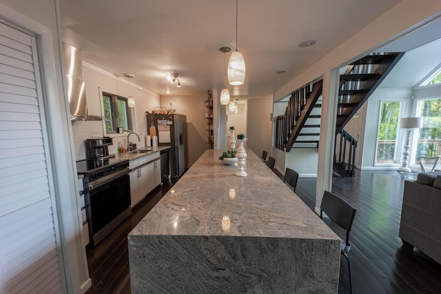 kitchen with appliances with stainless steel finishes, wall chimney exhaust hood, dark wood finished floors, a sink, and white cabinets