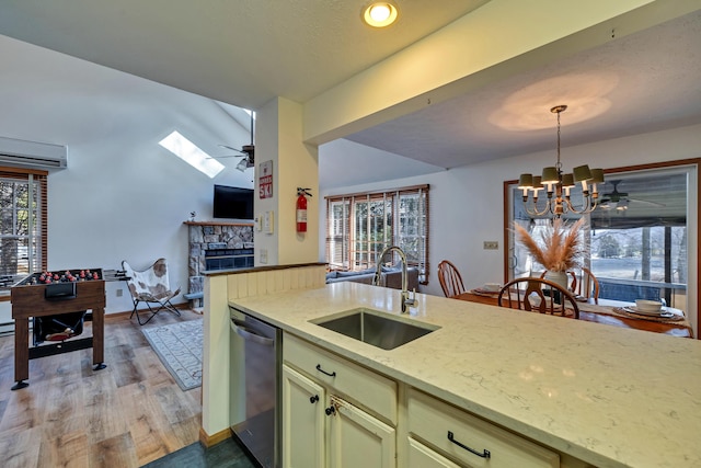 kitchen with ceiling fan with notable chandelier, a sink, stainless steel dishwasher, a fireplace, and hanging light fixtures