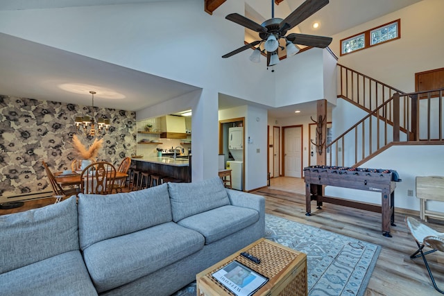 living area with ceiling fan with notable chandelier, baseboards, stairs, and light wood-style floors