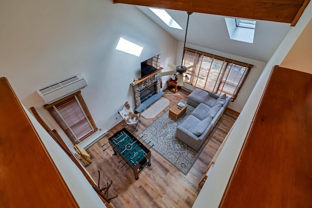 living room featuring a stone fireplace, vaulted ceiling with skylight, wood finished floors, and a wall mounted air conditioner