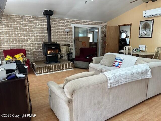 living room featuring lofted ceiling, a wall mounted AC, a wood stove, brick wall, and light hardwood / wood-style floors